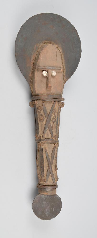 Ofo anam: a wooden ritual object with a carved human face and a broad disc-shaped head, the shaft bound with iron strips and ending in iron blades.