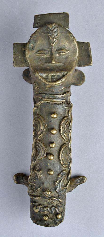 A brass ofo: a cylindrical cast object with anthropomorphic features, four supports, and elaborate geometric decoration.